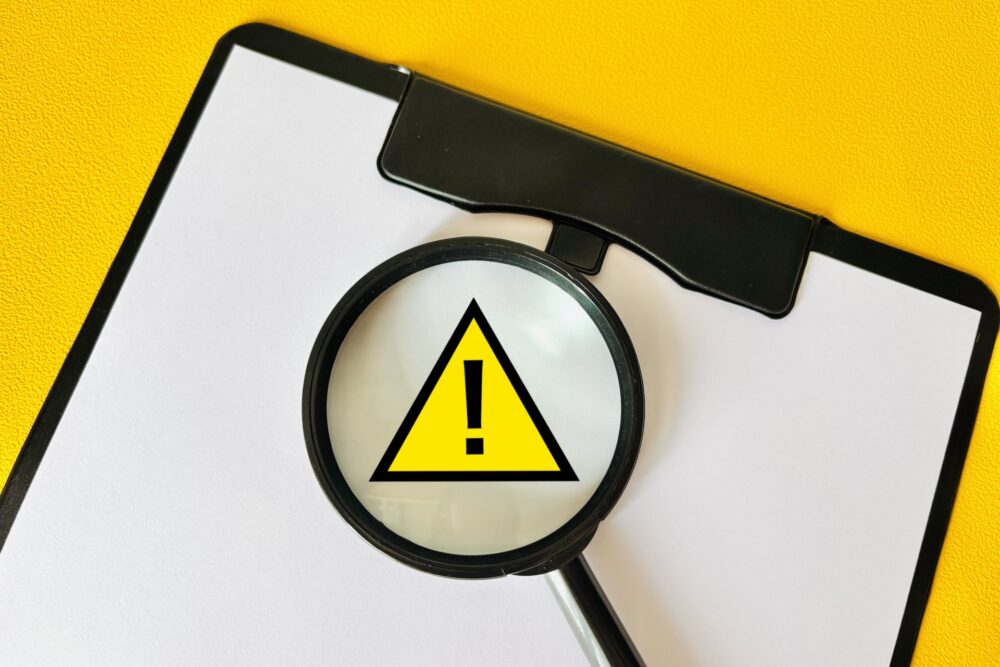 注意マークを虫眼鏡で拡大しているイメージ 注意マークを虫眼鏡で拡大しているイメージ